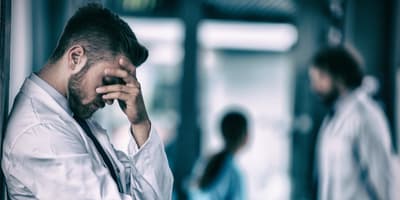 Healthcare worker holding his head in his hand in the hallway